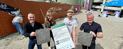 Vier Personen halten Auszeichnungen in der Hand. Im Hintergrund sprühen Leute Graffiti auf eine Schwabenwand. Weiterverlinkung auf eine Schwabenwand auf dem Gaswerkgelände Newsartikel