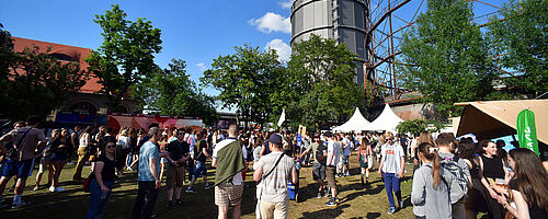 Menschen laufen auf dem Gaswerksgelände. Im Hintergrund ist der Gaskessel. Weiterverlinkung auf Modular 2022 Newsartikel