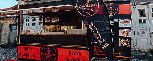 Frontansicht auf Balkan Kitchen mit Bannern und roten Teppich auf dem Boden. Weiterverlinkung auf The Balkan Kitchen Newsartikel