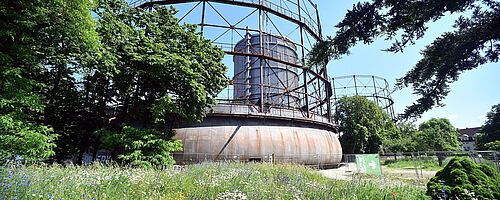 Grüne Wiese auf dem Gaswerksgelände. Im Hintergrund ist das Gaswerk. Ein Klick sorgt für eine Großansicht des Bildes. Weiterverlinkung auf Gaswerk Natur Kund und Kultur Newsartikel
