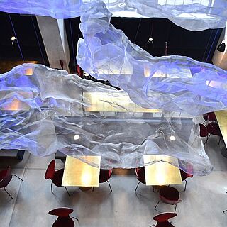 Beleuchtete Tische mit Stühlen. An den Decken hängen gebastelte Wolken. Weiterverlinkung auf Restaurant Bar Ofenhaus Seite