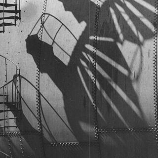Schwarz weiß Bild einer Wendeltreppe. Der Schatten auf der Wand stellt einen Schutzengel dar. Weiterverlinkung auf die Gaswerk Museum Seite