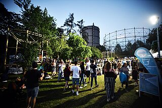 Menschenmenge läuft auf dem Gaswerksgelände. Im Hintergrund ist der Gaskessel