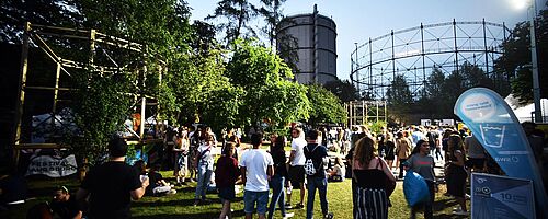 Menschenmenge läuft auf dem Gaswerksgelände. Im Hintergrund ist der Gaskessel. Weiterverlinkung auf Modular Anreise Newsartikel