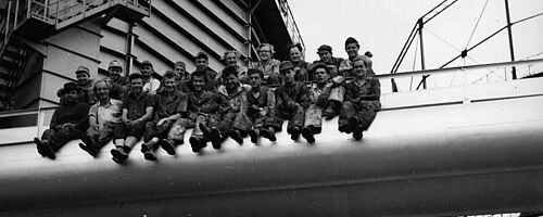 Arbeiter sitzen auf einer Röhre auf der Außenfassade des Gaswerks. Weiterverlinkung auf Industriedenkmal Newsartikel