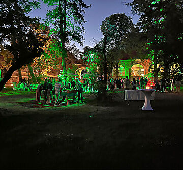 Menschen spielen Kicker auf der Wiese zwischen Festivalfläche und Trafostation. Im Hintergrund stehen Menschen mit Getränken. Ein Klick sorgt für eine Großansicht des Bildes