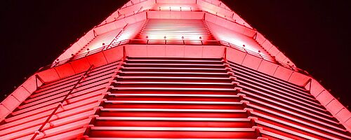 Rot beleuchteter großer Scheibengasbehälter. Weiterverlinkung auf Night of Light Newsartikel