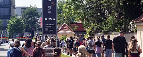 Leute laufen in einer Schlange auf das Gaswerksgelände. Weiterverlinkung auf Summerstage Gaswerk Newsartikel