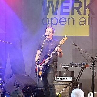 Musiker stehen auf einer Bühne und spielen Instrumente. Im Vordergrund sind Zuschauer. Weiterverlinkung auf Gaswerk Kulturschaffende Seite