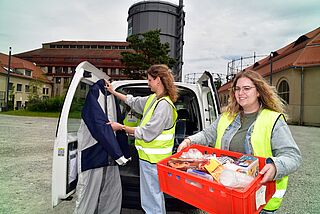 Zwei Mitarbeiterinnen des SKM Augsburg stehen vor dem Kältemobil und transportieren Spendenartikel