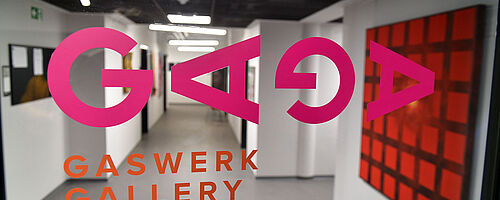 Flur mir Gemälden an der Wand. Im Vordergrund ist der Aufdruck "GAGA Gaswerk Gallery". Weiterverlinkung auf Gaswerk offene Ateliers 2024 Newsartikel