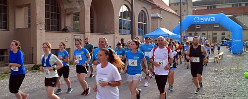 Läufer mit swa Trikot laufen beim swa Spendenlauf. Im Hintergrund ist das Ziel mit swa Branding