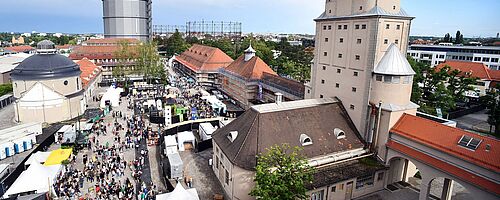 Luftaufnahme einer Menschenmenge mit verschiedenen Ständen auf dem Gaswerksgelände. Weiterverlinkung auf nächsten Schritte 2020 Newsartikel