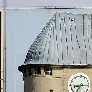 Blick auf Fensterfassade mit einer Reflektion eines Gebäudes mit Uhr. Weiterverlinkung auf Gaswerk Kulturschaffende Seite
