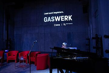 Pianist spielt auf einem Flügel. Im Hintergrund das Gaswerk Logo