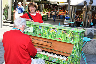 Mann spielt auf einem bemalten Klavier, Frau lehnt sich an das Klavier an. - Beim anklicken wird das Bild vergrößert.